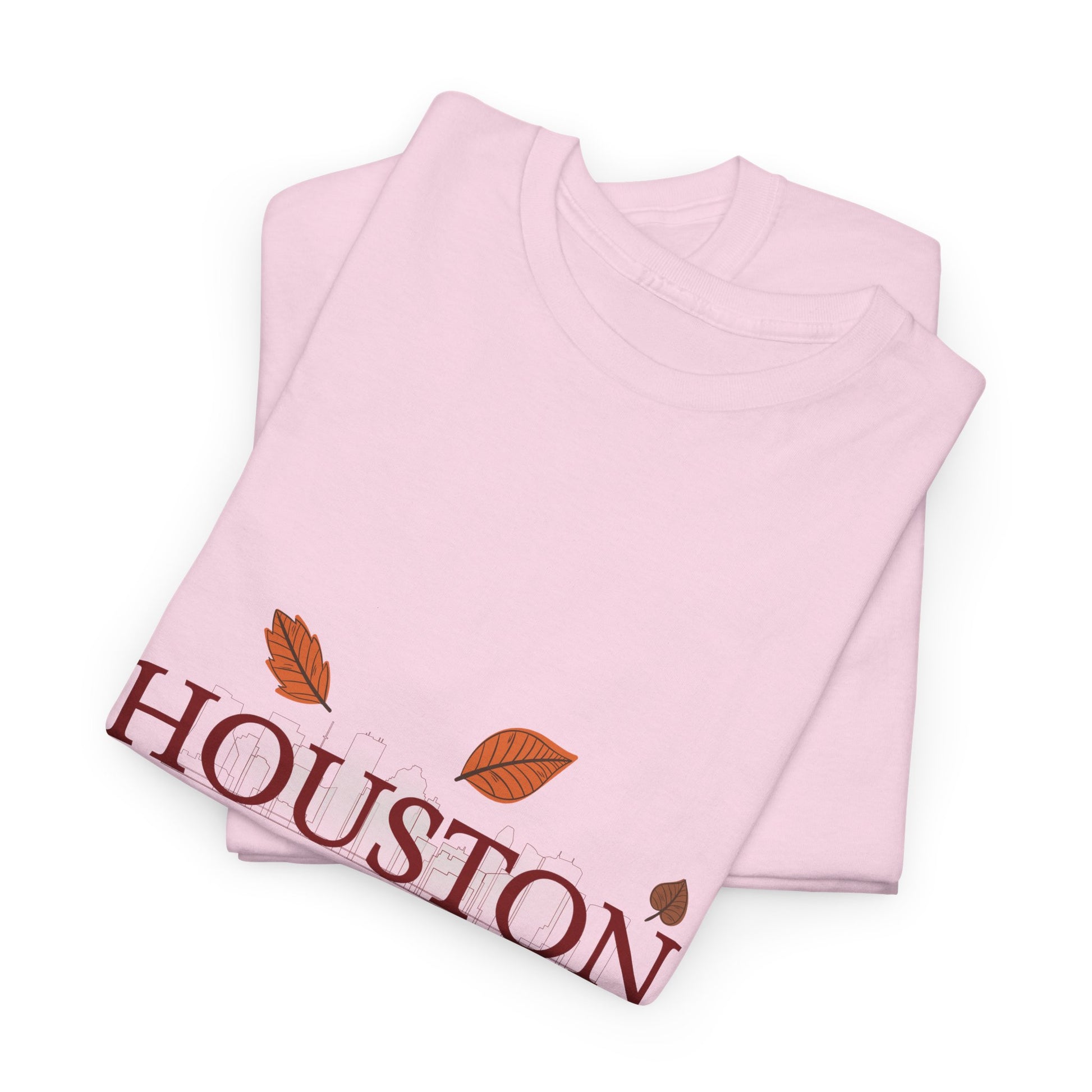Folded Pink t-shirt with 'Houston Temps Don't Fall' text and fall leaf graphics along with Houston skyline in the background